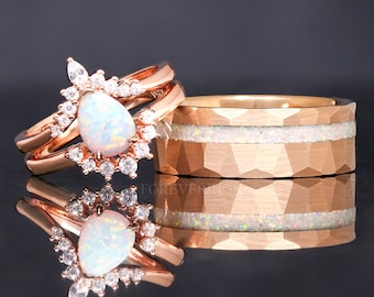 May include: A pair of rose gold wedding bands with a pear-shaped opal gemstone set in a halo of smaller diamonds. The band on the left is a delicate, double-band ring with a pear-shaped opal gemstone set in a halo of smaller diamonds. The band on the right is a thicker band with a hammered finish and a thin band of opal inlay.