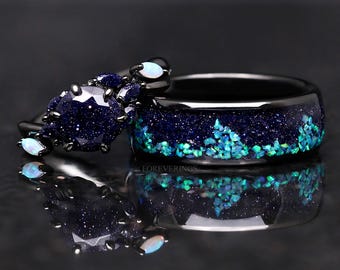 Puede incluir: Un anillo de banda negro con un diseño moteado azul y verde. El anillo está engastado con pequeñas piedras azules y verdes. La banda también está engastada con una piedra azul más grande. El anillo se empareja con un anillo de compromiso a juego con una piedra azul más grande y piedras blancas más pequeñas.
