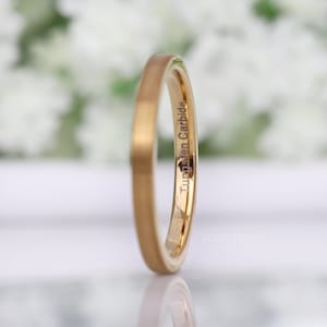 May include: A gold-colored tungsten carbide ring with a matte finish. The ring has the words "Tungsten Carbide" engraved on the side. The ring is a simple band design.