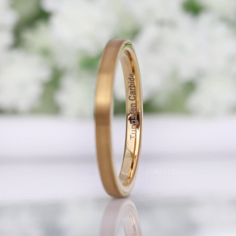 May include: A gold-colored tungsten carbide ring with a matte finish. The ring has the words "Tungsten Carbide" engraved on the side. The ring is a simple band design.