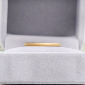 May include: A simple gold wedding band in a white velvet ring box. The band is smooth and has a matte finish.