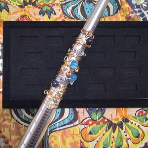 Puede incluir: Una herramienta de medición de tamaño de anillo de plata con una variedad de anillos de oro y plata con cuentas de colores. Los anillos están apilados en la herramienta y están listos para ser medidos.