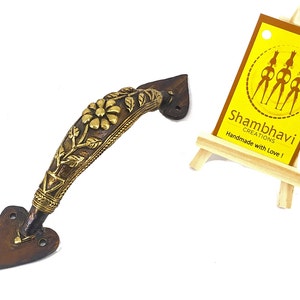 May include: Ornate bronze door handle with floral and leaf detailing. The handle has a heart-shaped base and a curved design. The image includes a small yellow tag with the text "Shambhavi Creations" and "Handmade with Love!"