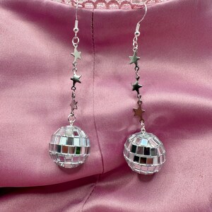 May include: Silver earrings with a disco ball charm and a chain of silver stars.