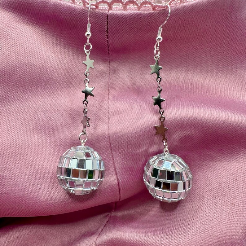 May include: Silver earrings with a disco ball charm and a chain of silver stars.