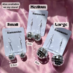 May include: Three pairs of silver disco ball earrings on white cards with the text "Made by Samantha" and the size of the earrings: "Small", "Medium", and "Large". The earrings are 2.3 cm, 3 cm, and 4 cm in diameter.