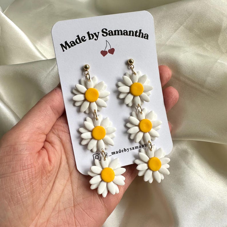 May include: White daisy earrings with yellow centers. The earrings are made of polymer clay and have a gold hook.