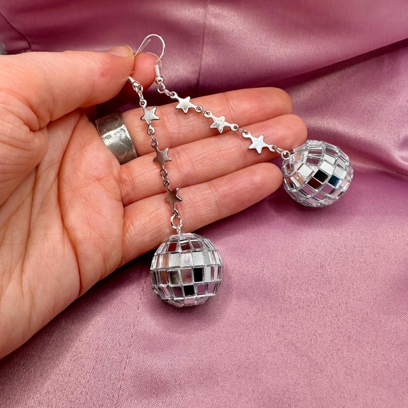 May include: A pair of silver dangle earrings with a disco ball charm and a chain of silver stars.
