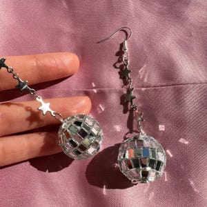 May include: A pair of silver disco ball earrings with a dangling chain of stars. The disco balls are made of small mirrored tiles.