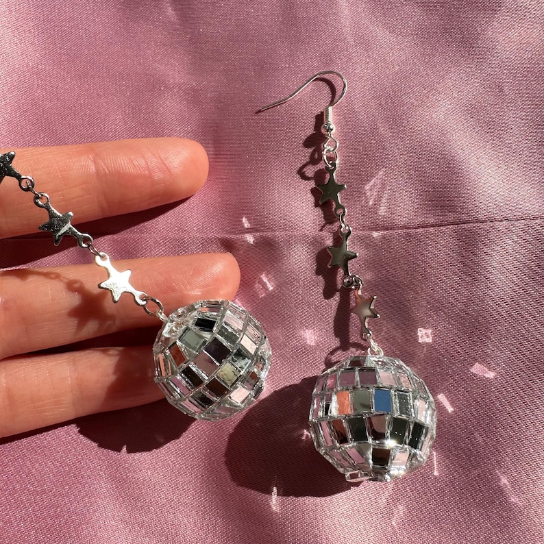 May include: A pair of silver disco ball earrings with a dangling chain of stars. The disco balls are made of small mirrored tiles.