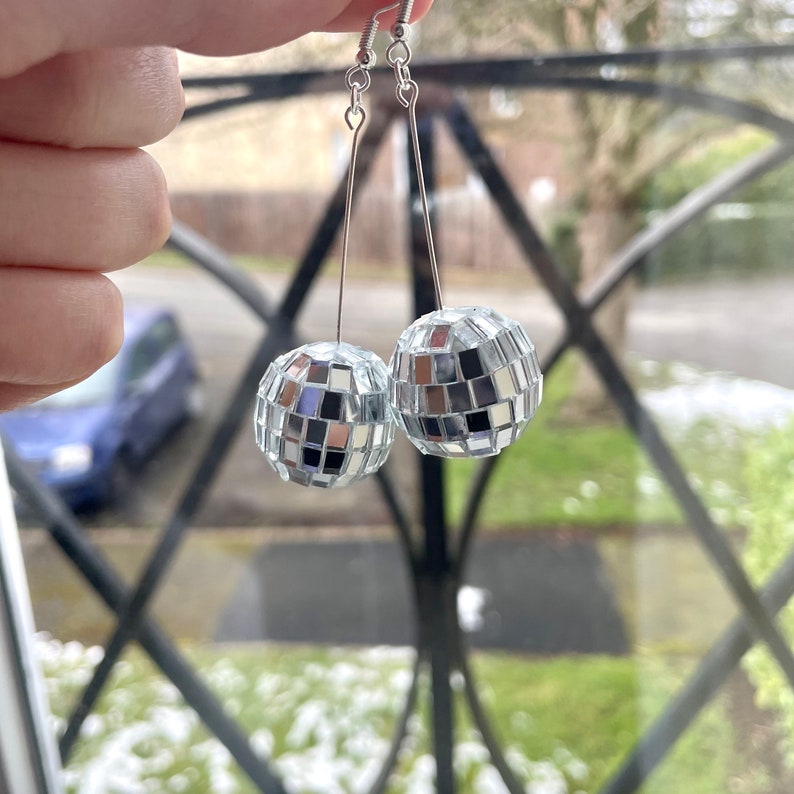 May include: A pair of silver disco ball earrings. Each earring features a round, mirrored ball with small, square tiles.