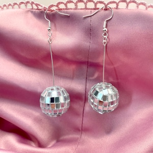 May include: A pair of silver dangle earrings with disco ball charms. The disco balls are made of small mirrored tiles.