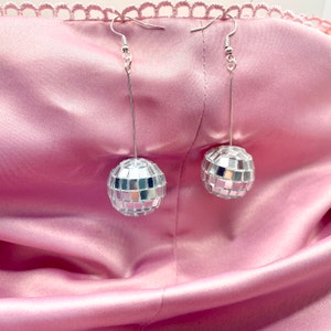 May include: A pair of silver disco ball earrings hanging from a pink fabric background.