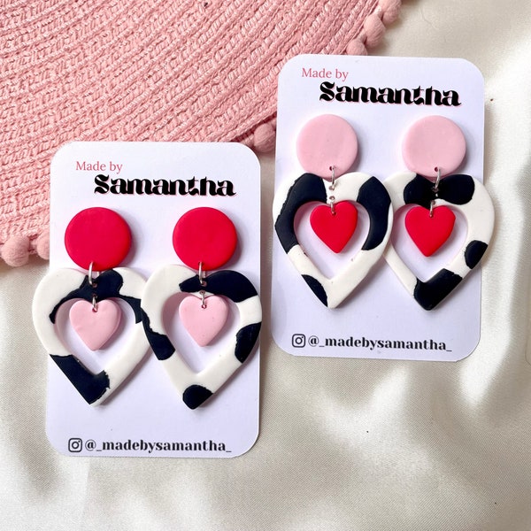 Cut out heart shaped polymer clay cow print earrings with pink and red details and charm