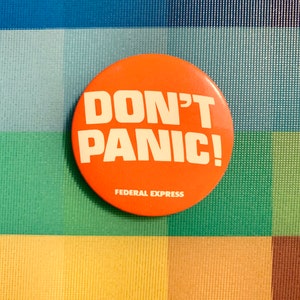 May include: Orange button with the text "DON'T PANIC!" in white lettering. The button has the words "FEDERAL EXPRESS" printed in white at the bottom.