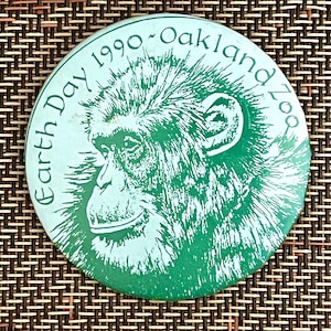 以下が含まれることがあります： チンパンジーの顔と「Earth Day 1990 Oakland Zoo」という文字が書かれた緑と白のボタン。