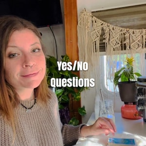 May include: A woman wearing a beige sweater sits at a table with a deck of tarot cards. The text "yes/no questions" is visible in the image.