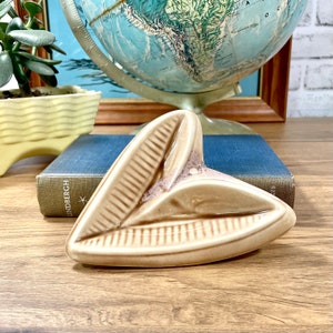 May include: A brown ceramic ashtray shaped like a leaf. The ashtray has a textured surface and a small hole in the center.
