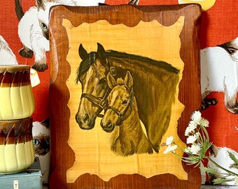 Pode incluir: Uma placa de madeira com uma ilustração vintage de dois cavalos, um marrom e outro branco, sobre um fundo amarelo. A placa tem uma moldura de madeira marrom.