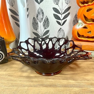 Könnte beinhalten: Eine dunkelrote Glasschale mit einem zarten, durchbrochenen Design. Die Schale steht auf einer Holzoberfläche.