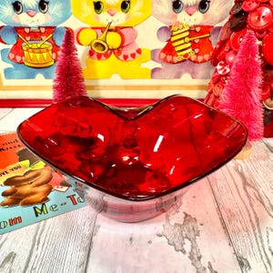 Może przedstawiać: Czerwona szklana miska w kształcie serca. Miska stoi na drewnianej powierzchni.