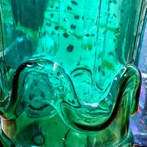 May include: A teal blue glass bottle with a textured, wavy design. The bottle is empty and has a wide mouth.