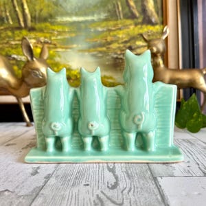 May include: A set of three ceramic mugs with a speckled, cream-colored glaze. Each mug features a different hand-painted design: a blue and green leaf, a yellow flower, and a red berry. The mugs have a simple, rounded shape.