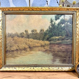 May include: A framed landscape painting depicting a river scene with trees and foliage in shades of green and brown. The river is a light blue-green color and the sky is a pale pink. The painting is signed "R.H. Z. 1927" in the lower right corner.