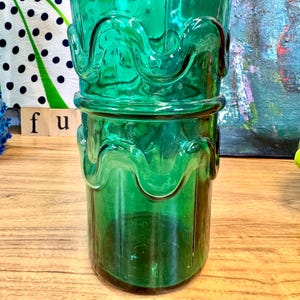May include: A tall, green glass vase with a wavy, textured design. The vase has a wide mouth and a narrow base.