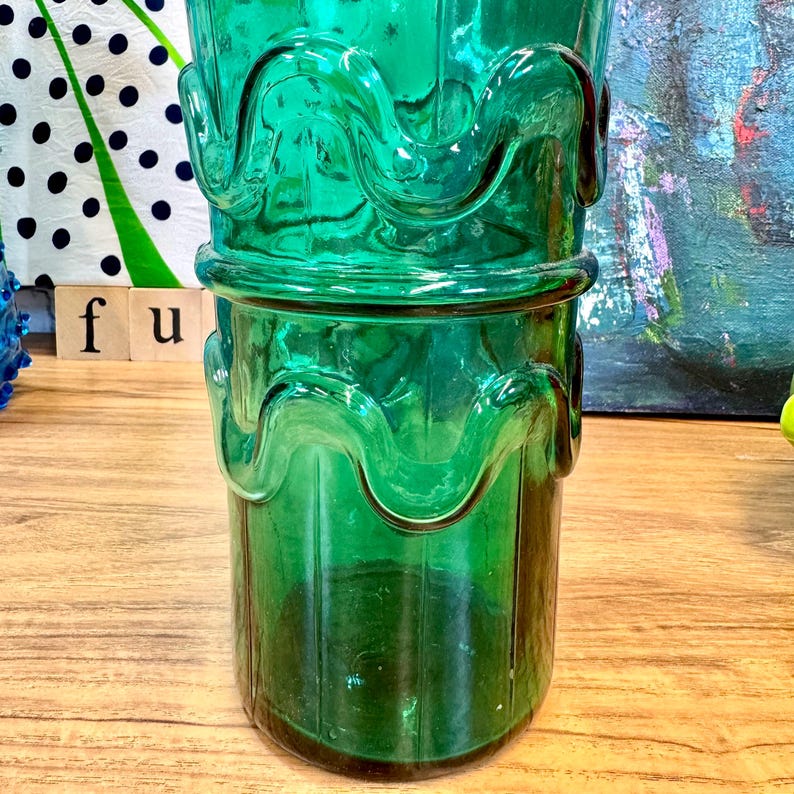 May include: A tall, green glass vase with a wavy, textured design. The vase has a wide mouth and a narrow base.