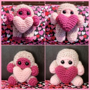 May include: Four crocheted plush toys in the shape of a pink and purple creature holding a pink heart. The toys are sitting on a background of pink hearts.