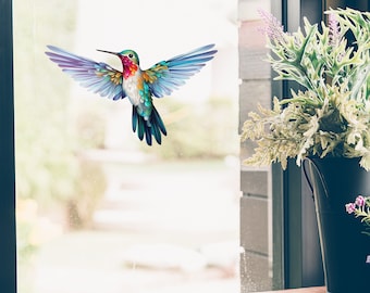 Puede incluir: Una calcomanía de ventana de colibrí colorida con plumas azules, verdes, moradas y rojas. El colibrí está en vuelo con las alas extendidas.
