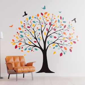 Könnte beinhalten: Eine schwarze Silhouette eines Baumes mit bunten Blättern an einer weißen Wand. Der Baum hat einen dicken Stamm und Äste, die sich zu den Seiten erstrecken. Die Blätter sind in Rot-, Orange-, Gelb-, Grün- und Blautönen gehalten. Es gibt auch kleine schwarze Silhouetten von Vögeln, die um den Baum fliegen.