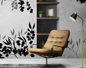 May include: A brown leather armchair with a black metal frame sits in a room with a gray wall featuring black silhouette floral designs. A black and gold floor lamp stands to the right of the chair.