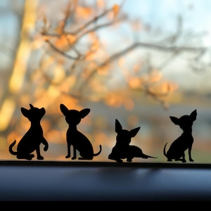 May include: Four black silhouette decals of chihuahua dogs in various poses. The decals are placed on a car dashboard against a blurred background of a tree and sky.
