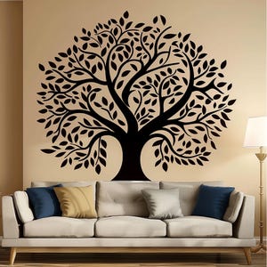 May include: A black tree wall decal with detailed leaves, displayed on a beige wall above a beige sofa with blue and gold cushions. A floor lamp with a white shade is positioned to the right.