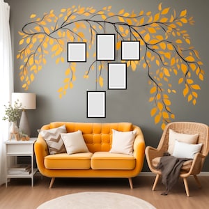 May include: A yellow velvet sofa with cushions sits in front of a grey wall with a painted black branch with yellow leaves and five black picture frames hanging from the branch.