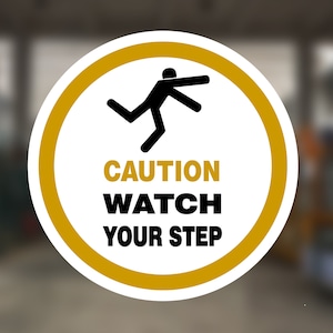 May include: A round yellow and white caution sign with a black stick figure falling down. The sign reads "CAUTION WATCH YOUR STEP".