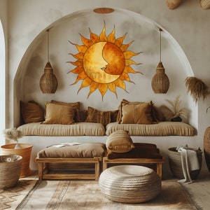Peut inclure: Un salon de style bohème avec un canapé beige et deux poufs en bois. Le mur derrière le canapé présente un grand motif soleil et lune en aquarelle avec un visage. La pièce est décorée de plantes et de paniers en osier.