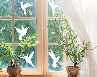 Puede incluir: Una ventana con siluetas blancas de colibríes en el cristal. Dos plantas en maceta con hojas verdes están en el alféizar de la ventana. La ventana está parcialmente cubierta por una cortina blanca transparente.