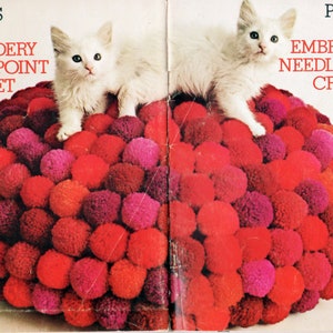 Può includere: Due gattini bianchi sono seduti su un cuscino a forma di cuore fatto di pompon rossi, rosa e arancioni. Il cuscino è circondato da altri pompon. La copertina del libro recita "Pillows in Embroidery Needlepoint Crochet Knit Coats & Clarks Book No. 209 35¢".