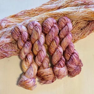 May include: Four skeins of hand-dyed yarn in shades of pink, white, and orange. The yarn is a speckled, variegated colorway.
