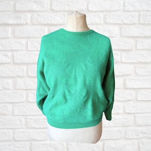 May include: A bright green sweater with a crew neck and long sleeves. The sweater has a subtle, textured pattern across the front. The garment is displayed on a mannequin against a white brick wall background. A casual, everyday top.