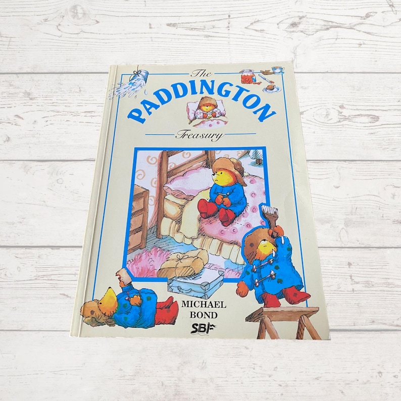 Pode incluir: A capa do livro "The Paddington Treasury" apresenta uma ilustra&ccedil;&atilde;o colorida de Paddington Bear com um casaco azul e botas vermelhas. O t&iacute;tulo do livro &eacute; "The Paddington Treasury" e o autor &eacute; Michael Bond.