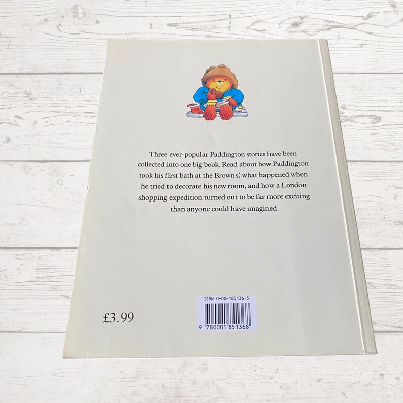 Pode incluir: Uma capa de livro com Paddington Bear vestindo um casaco vermelho e um chap&eacute;u azul. O t&iacute;tulo do livro &eacute; "Paddington" e o texto na contracapa descreve o livro como uma cole&ccedil;&atilde;o de tr&ecirc;s hist&oacute;rias de Paddington. O n&uacute;mero ISBN &eacute; 0-00-185136-5.