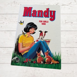 May include: A vintage "Mandy" comic book cover from 1986. It shows a girl in a yellow top and blue trousers reading a comic with a dog and two rabbits. The title "Mandy" is in red, with the text "FOR GIRLS" and the year 1986.