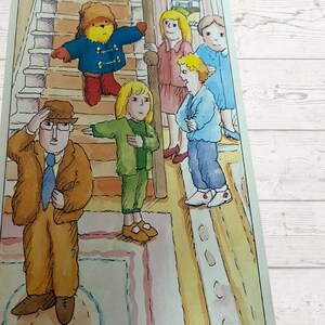 Pode incluir: Uma ilustra&ccedil;&atilde;o em aquarela de um grupo de crian&ccedil;as e um urso de peluche em p&eacute; em uma escada. As crian&ccedil;as est&atilde;o vestindo roupas coloridas e o urso de peluche est&aacute; vestindo um casaco azul. Um homem de terno marrom e chap&eacute;u est&aacute; em p&eacute; na parte inferior das escadas.
