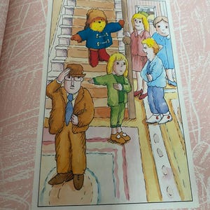 Pode incluir: Um grupo de crian&ccedil;as e um homem de terno marrom e chap&eacute;u est&atilde;o em uma sala com uma escada. Um urso de pel&uacute;cia vestindo um casaco azul est&aacute; na escada. As crian&ccedil;as est&atilde;o vestindo roupas coloridas.