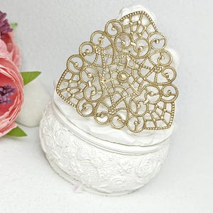 May include: A gold filigree design in the shape of a triangle, sitting on top of a white ceramic box with a floral design.