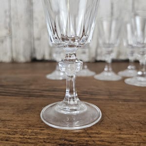 Könnte beinhalten: Klare Weingläser aus Kristall mit detailliertem, facettiertem Design. Das Glaswaren hat einen runden Fuß, einen dekorativen Stiel und eine ausgestellte Schale. Die Gläser sind auf einer Holzoberfläche angeordnet, mit einem unscharfen Hintergrund.